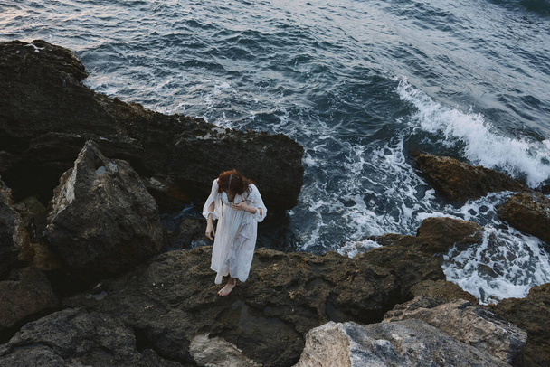Woman in a white dress with wet hair stands on a cliff top view - Foto, imagen