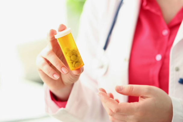 Medico tenere contenitore di plastica pieno di minuscole pillole bianche, stagista femminile pubblicizza farmaci - Foto, immagini