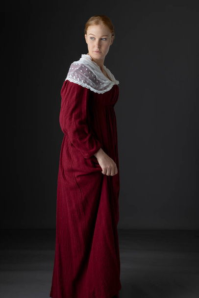 Una donna Regency indossa un abito di lino rosso con uno scialle bianco in pizzo modestia sullo sfondo di uno studio - Foto, immagini