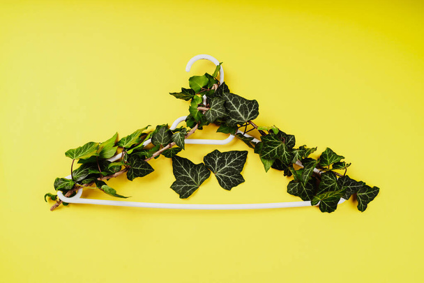 Hangers entwined with plants on yellow background with copy space.Conscious and environmentally friendly consupmtion in shopping.Zero waste.Shopping,sale,promo, concept.Top view flat lay copy space - Photo, Image