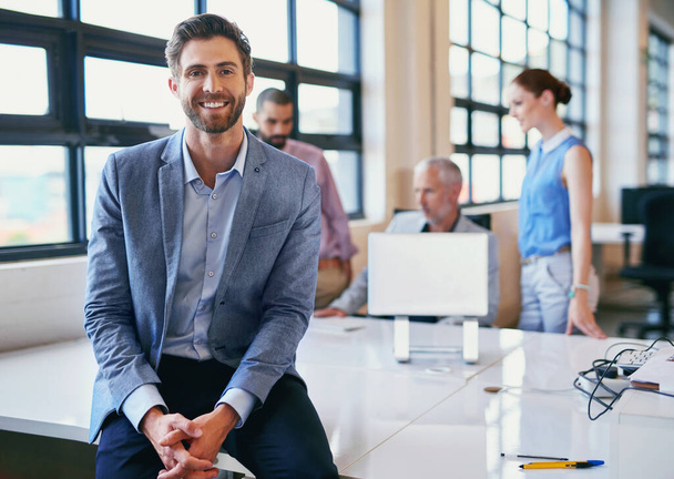 Hes the face of job satisfaction. Portrait of a confident businessman posing in the office with his colleagues in the background. - Photo, Image