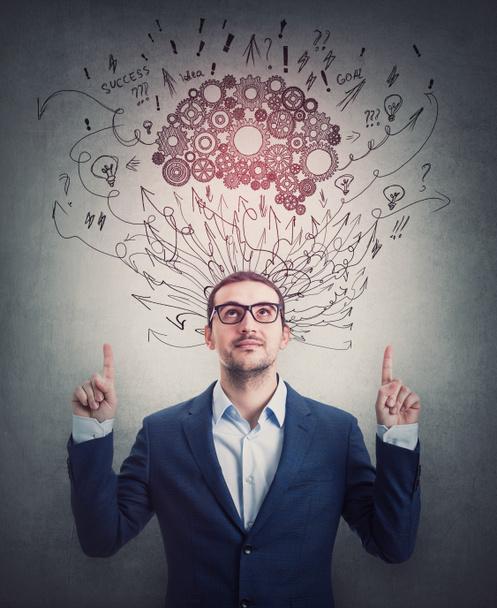 Contented businessman pointing up forefingers, looking satisfied. Cogwheel brain and sketches as thoughts over head. Confident business person, mental development concept - Photo, Image