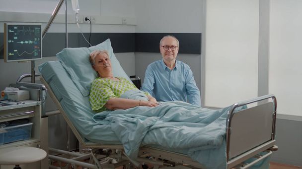 Portrait of pensioner with disease laying in bed and man giving assistance - Foto, Imagem