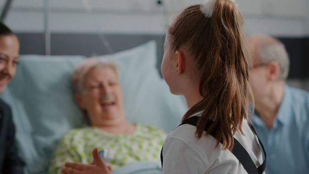 Крупним планом маленька дівчинка розмовляє з хворою пацієнткою в ліжку під час сімейного візиту
 - Фото, зображення