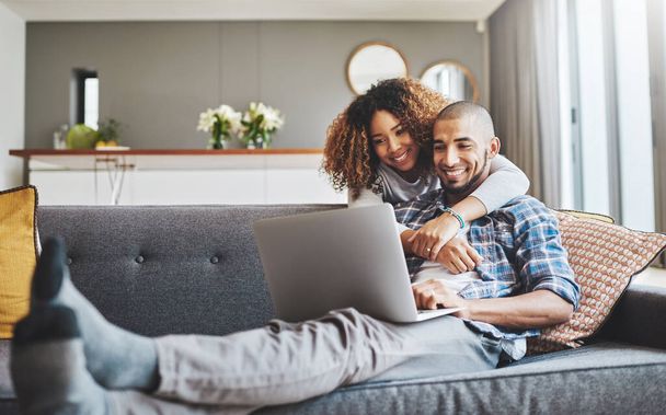 Theres no denying their connection. Shot of a young woman hugging her husband while he uses a laptop on the sofa at home. - Foto, Imagen