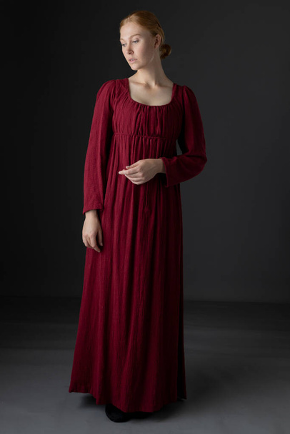 Una donna della classe operaia Regency che indossa un semplice abito di lino rosso sullo sfondo di uno studio - Foto, immagini