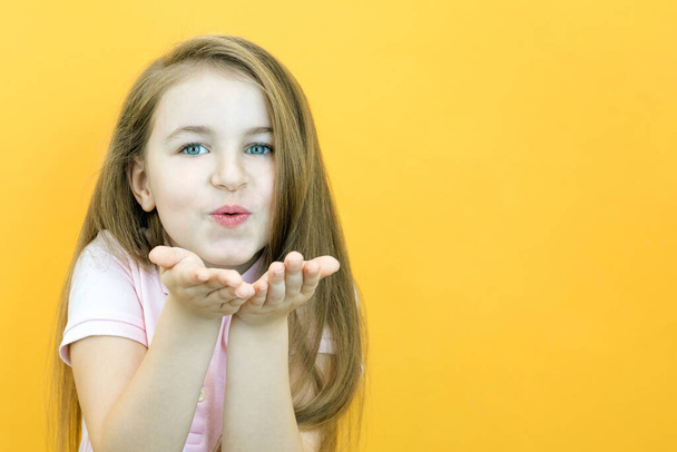 Little cute girl blows an air kiss directly to the camera on a yellow background. - Photo, image
