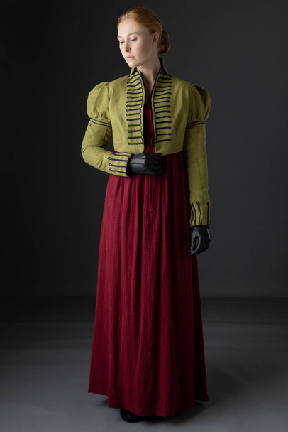 A Regency woman wearing a red linen dress with a green braided spencer and gloves against a studio backdrop - Photo, image