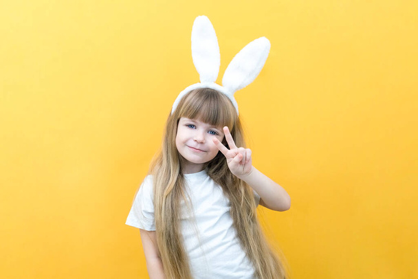 cheerful girl with rabbit ears on her head on a yellow background. Funny crazy happy child. hands like a rabbit. Preparation for the Easter holiday. copy space for text, mockup - Фото, зображення