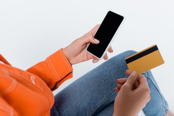 vista recortada de la mujer sosteniendo teléfono inteligente con pantalla en blanco y tarjeta de crédito aislada en gris - Foto, imagen