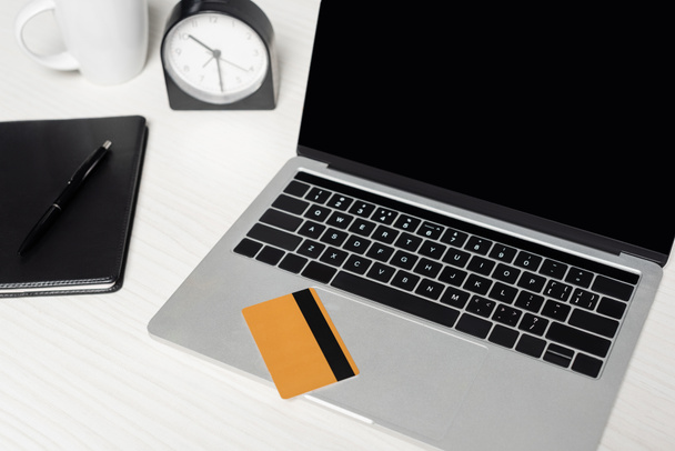 karta kredytowa na laptopie z pustym ekranem w pobliżu notebooka i kubka na białym biurku - Zdjęcie, obraz