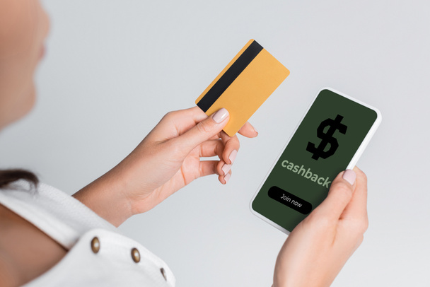 частковий вид жінки за допомогою мобільного телефону з кешбек на екрані і тримання кредитної картки ізольовано на сірому
  - Фото, зображення