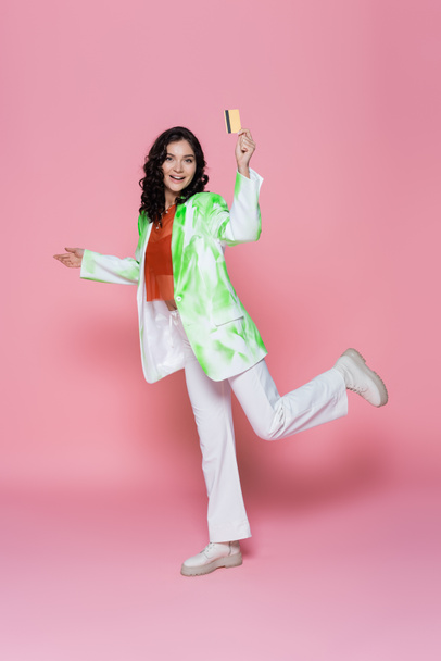 full length of happy young woman in tie-dye blazer holding credit card on pink  - Photo, Image