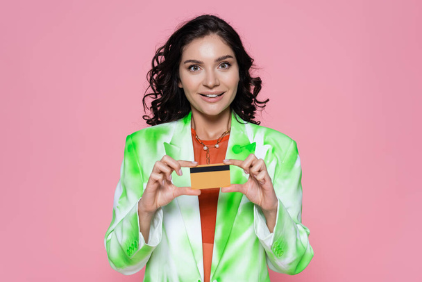 cheerful young woman in tie-dye blazer holding credit card isolated on pink  - Foto, immagini
