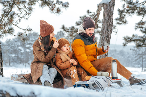 Famiglia felice con tazze di tè caldo trascorrere del tempo insieme nella foresta invernale - Foto, immagini