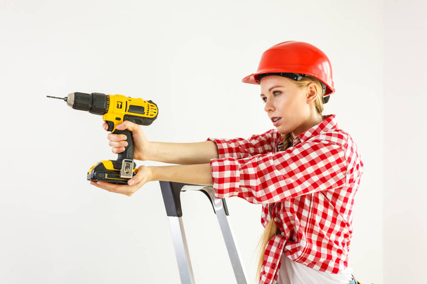Young determinated woman using drill doing home renovation. Female construction worker having driller tool drilling wall. - Fotografie, Obrázek