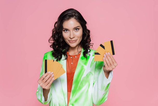 positive woman in green tie dye blazer holding credit cards and smiling isolated on pink - Photo, Image