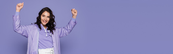excitée jeune femme en imperméable debout avec les mains levées isolé sur violet, bannière - Photo, image
