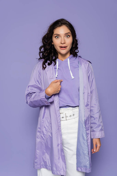 amazed young woman in raincoat pointing at herself isolated on purple - Photo, Image