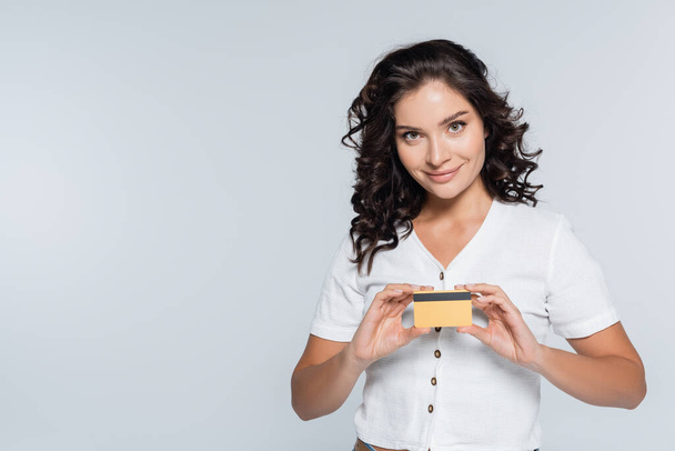 усміхнена і брюнетка жінка тримає кредитну картку ізольовано на сірому
 - Фото, зображення