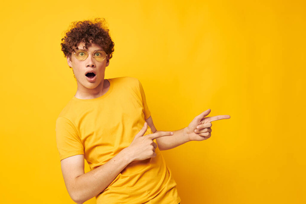 Young curly-haired man wearing stylish glasses yellow t-shirt posing isolated background unaltered - Foto, Bild
