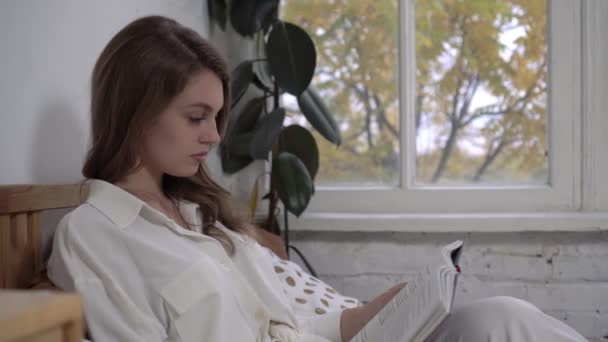 La joven está leyendo un libro en la cama. Mañana de otoño, hermosa mujer lee un libro en casa - Imágenes, Vídeo