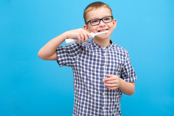 Een jongen met een bril poetst zijn tanden. Een klein kind met een tandenborstel op een blauwe achtergrond - Foto, afbeelding