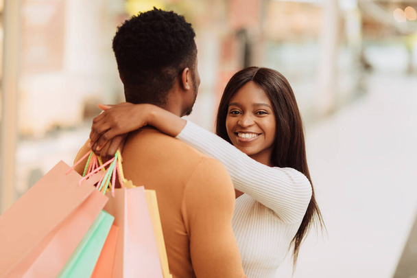 Alegre jovem casal preto abraçando e segurando sacos de compras - Foto, Imagem