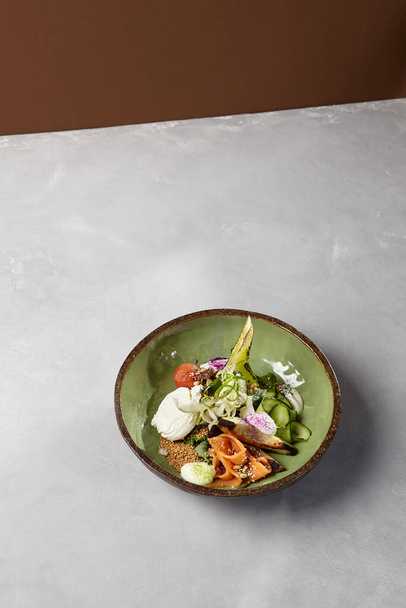 Salad bowl with salmon, avocado, broccoli, vegetables and egg on homemade ceramic plate. Buddha bowl with salmon, broccoli, quinoa in modern serveware. Modern ceramic dishware on concrete background - Foto, Imagem