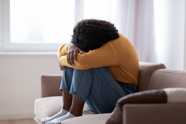 jonge zwarte vrouw met depressie huilen op bank thuis - Foto, afbeelding