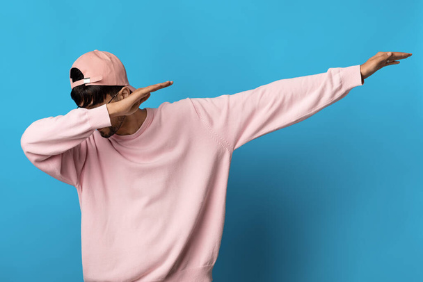 Millennial Kerl in rosa Sweatshirt und Mütze tupft auf blauem Hintergrund - Foto, Bild