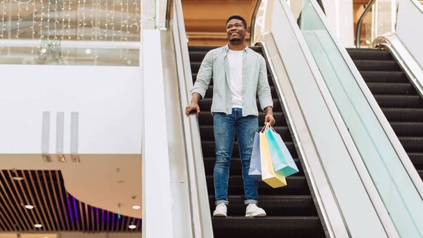 Šťastný černošky muž drží nákupní tašky děje na eskalátoru - Fotografie, Obrázek