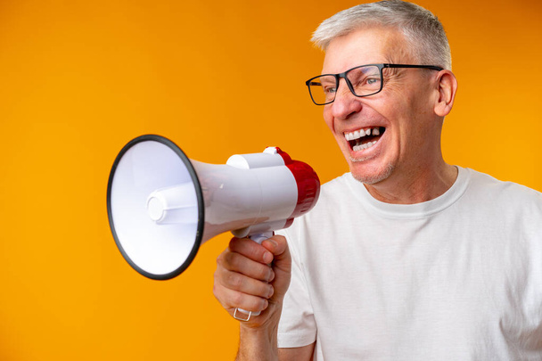 Portrait of mature man shouting with megaphone against yellow background - Zdjęcie, obraz