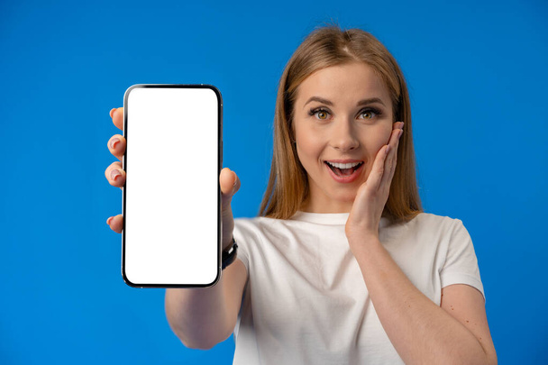 Young woman point finger at isolated smartphone screen over blue color background - Foto, Imagem