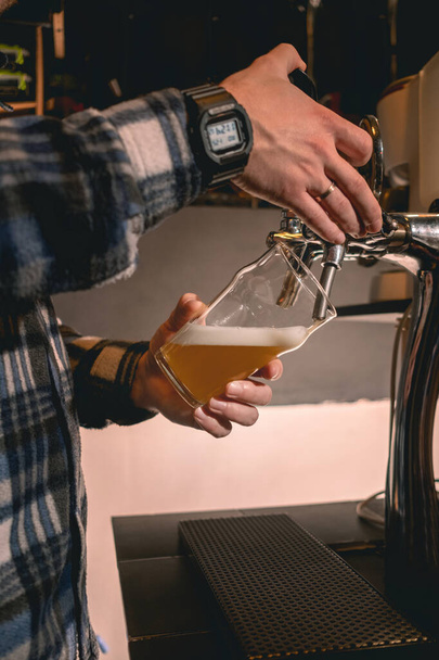 Barman staat achter bar teller vullen glas met wit bier uit de kraan - Foto, afbeelding