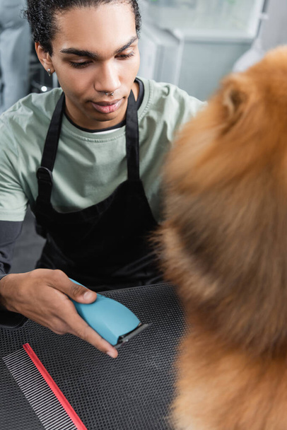 african american groomer holding electric trimmer near blurred dog - Foto, afbeelding