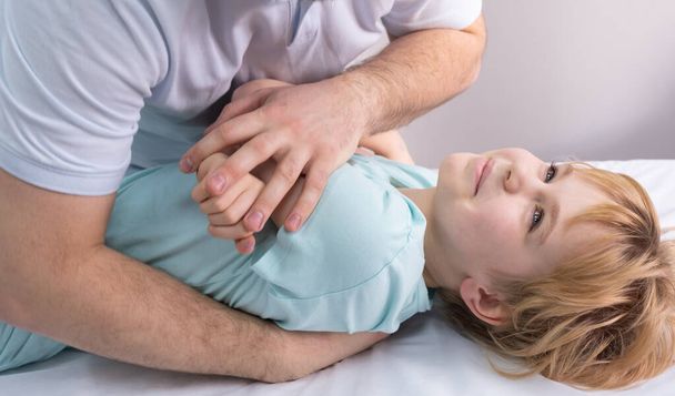An osteopath works with the child. Work with the chest, shoulders and spine. There is a teenage child on the couch. The doctor puts pressure on the patients chest. Posture correction - Foto, imagen