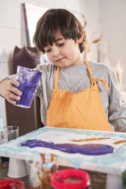 Child holding paints at the glass and painting on the canvas while spending time at the art school - Fotoğraf, Görsel