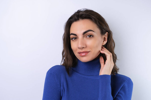 Young woman in a blue golf turtleneck on a white background looking at the camera with a confident smile - Zdjęcie, obraz