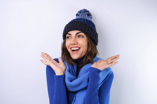 Young woman in a blue golf turtleneck, hat and scarf, on a white background, cheery in a good mood - Valokuva, kuva