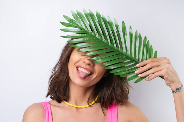 Summer portrait of young woman in pink swimsuit, bright yellow beach necklace with monstera palm leaf - Fotó, kép