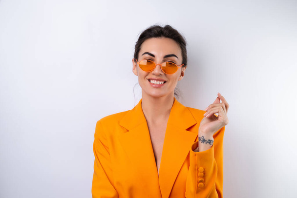 Giovane donna in occhiali alla moda e una giacca oversize arancione brillante su uno sfondo bianco - Foto, immagini