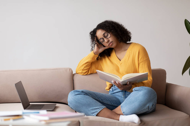 Moe jonge zwarte vrouw slapen met boek in de buurt laptop computer thuis, kopiëren ruimte - Foto, afbeelding