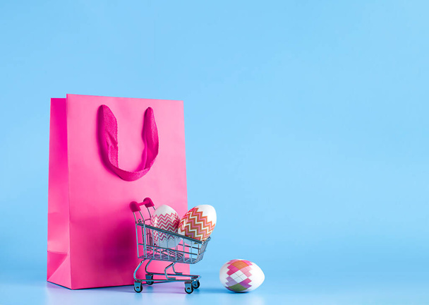 Easter banner, gift bag and shopping cart on a blue background. The concept of Easter sale, shopping, delivery of goods for the holiday - Photo, image