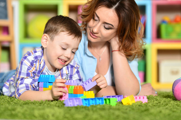 Woman and son playing with colorful plastic blocks on floor  - Foto, afbeelding