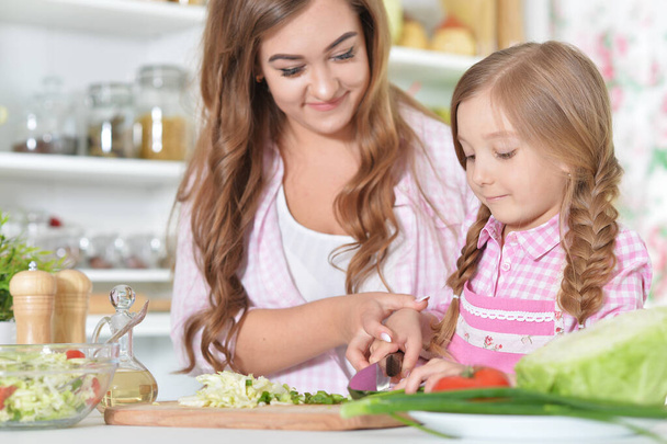 Girl with her mother cooking salad together at kitchen table  - Photo, Image