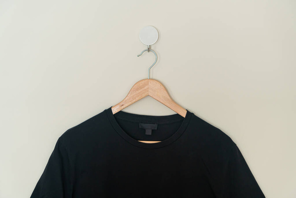 black t-shirt hanging with wood hanger on wall - Foto, afbeelding