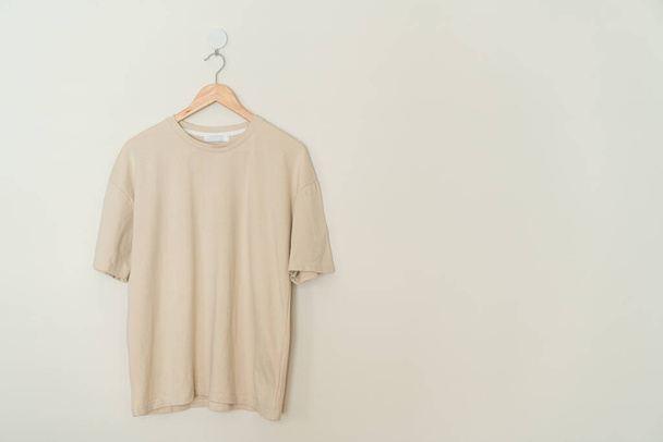 beige t-shirt hanging with wood hanger on wall - Photo, Image