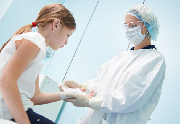 female surgeon doctor, in focus, bandaging childs hand in clinic - Φωτογραφία, εικόνα