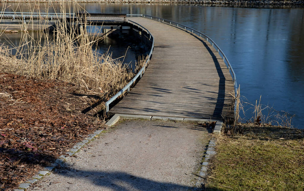 Schwimmender Steg aus Holzplanken, Seebrücke, enge, geschwungene Wege auf Stelzen, die über dem Seewasser auf den Grund getrieben werden. hat kein Geländer. mehr Design-Bürgersteig mit niedrigem Geländer für Rollstuhlfahrer - Foto, Bild